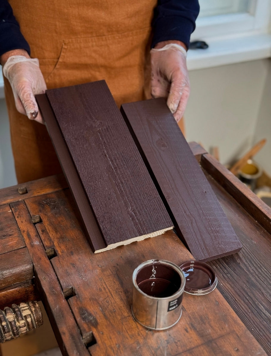 A person holding wooden boards painted with Paint Eco natural linseed oil paint in Aronia shade, with an open can beside them.