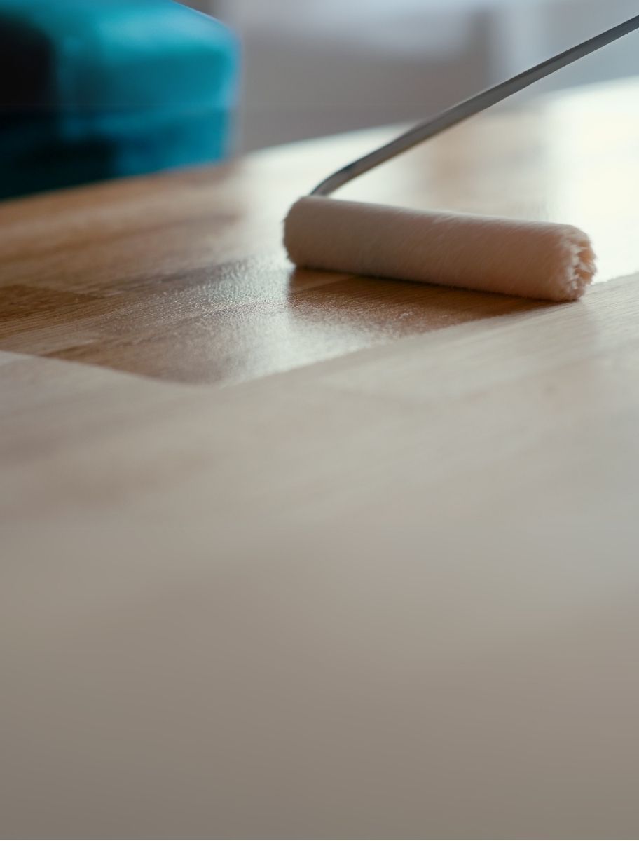 A wooden surface being coated with a matt hard wax coating finish using a roller, enhancing durability and natural beauty.