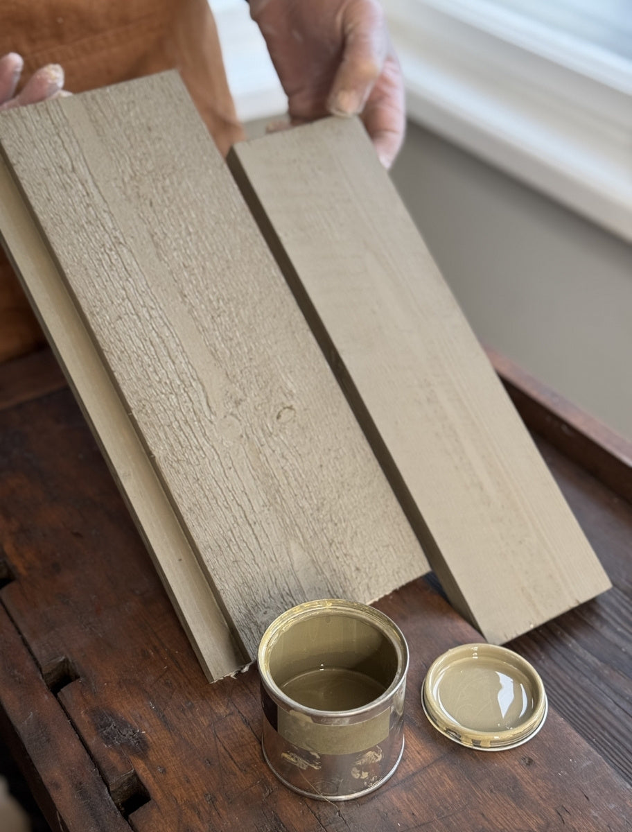 A person holding wooden boards painted with Paint Eco natural linseed oil paint in Olive shade, with an open can beside them.