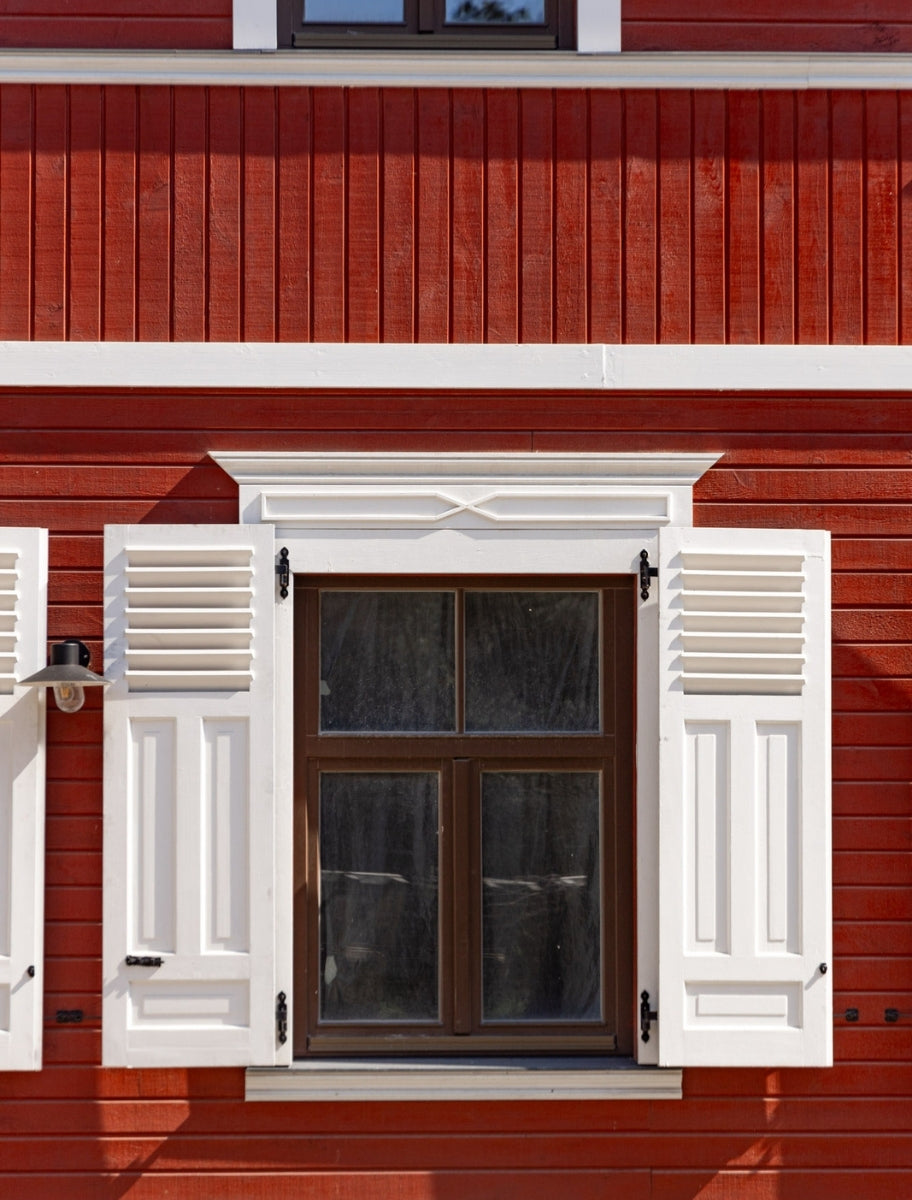 A finished wooden house exterior with Swedish Red Linseed Oil Paint, featuring white-framed windows.