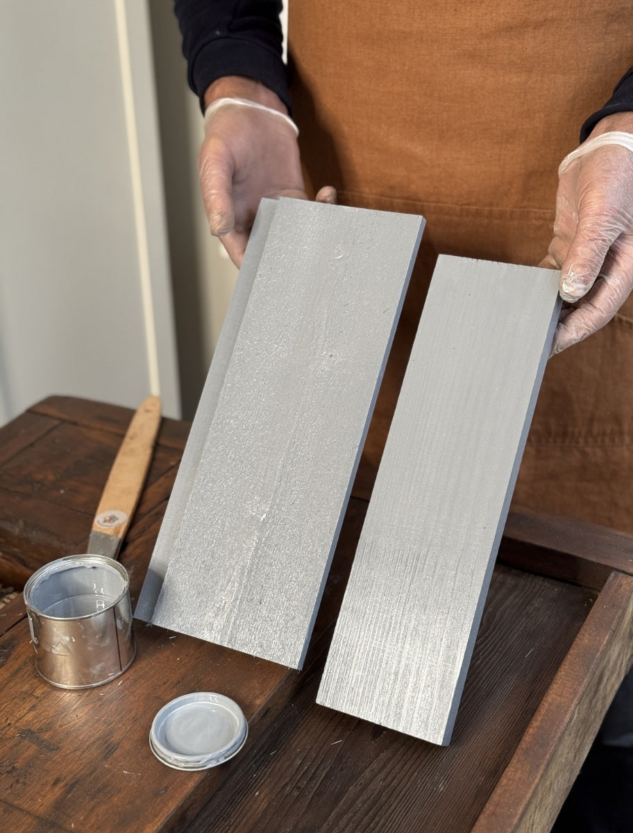 A person holding wooden boards painted with Paint Eco natural linseed oil paint in Gooseshade, with an open can beside them.