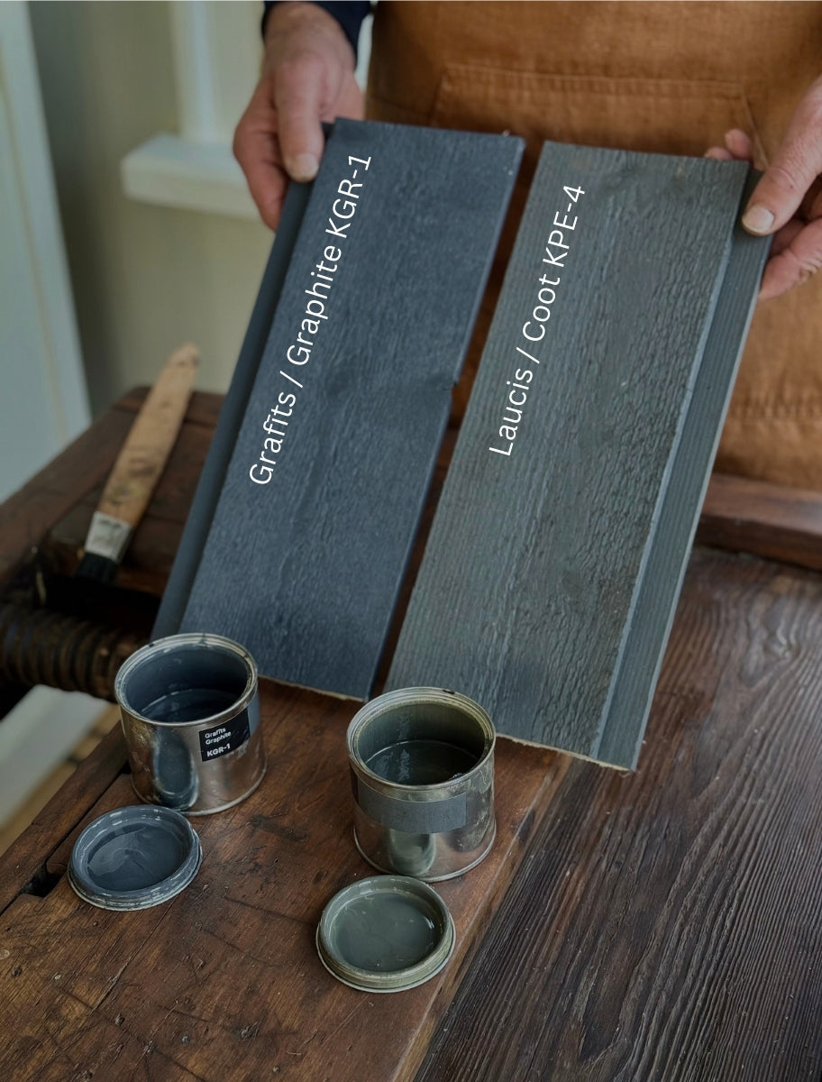 A person holding wooden boards painted with Paint Eco natural linseed oil paint in Graphite and Coot shade, with an open cans beside them.
