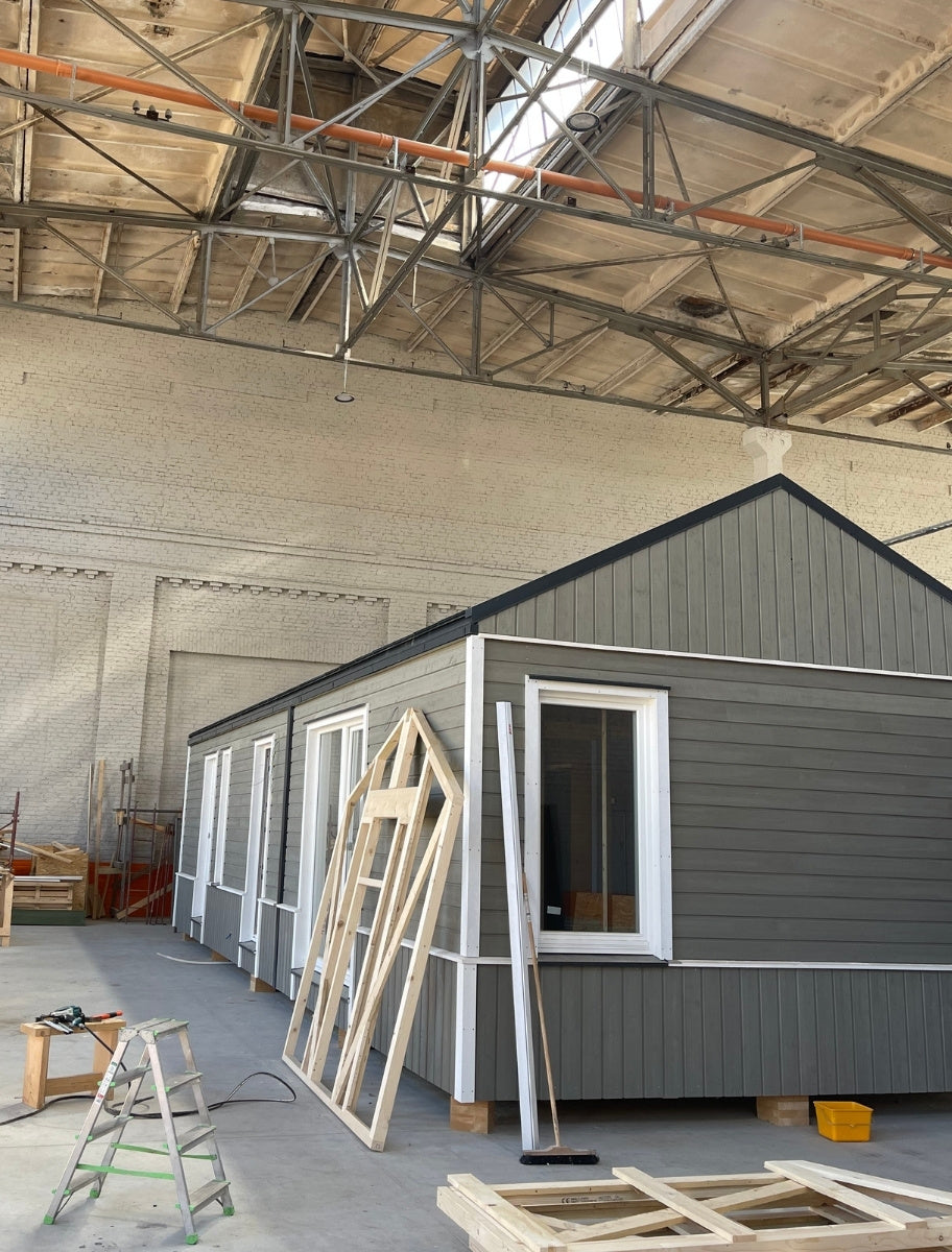A wooden house under construction, partially painted in a grayish-green shade using Paint Eco paint.