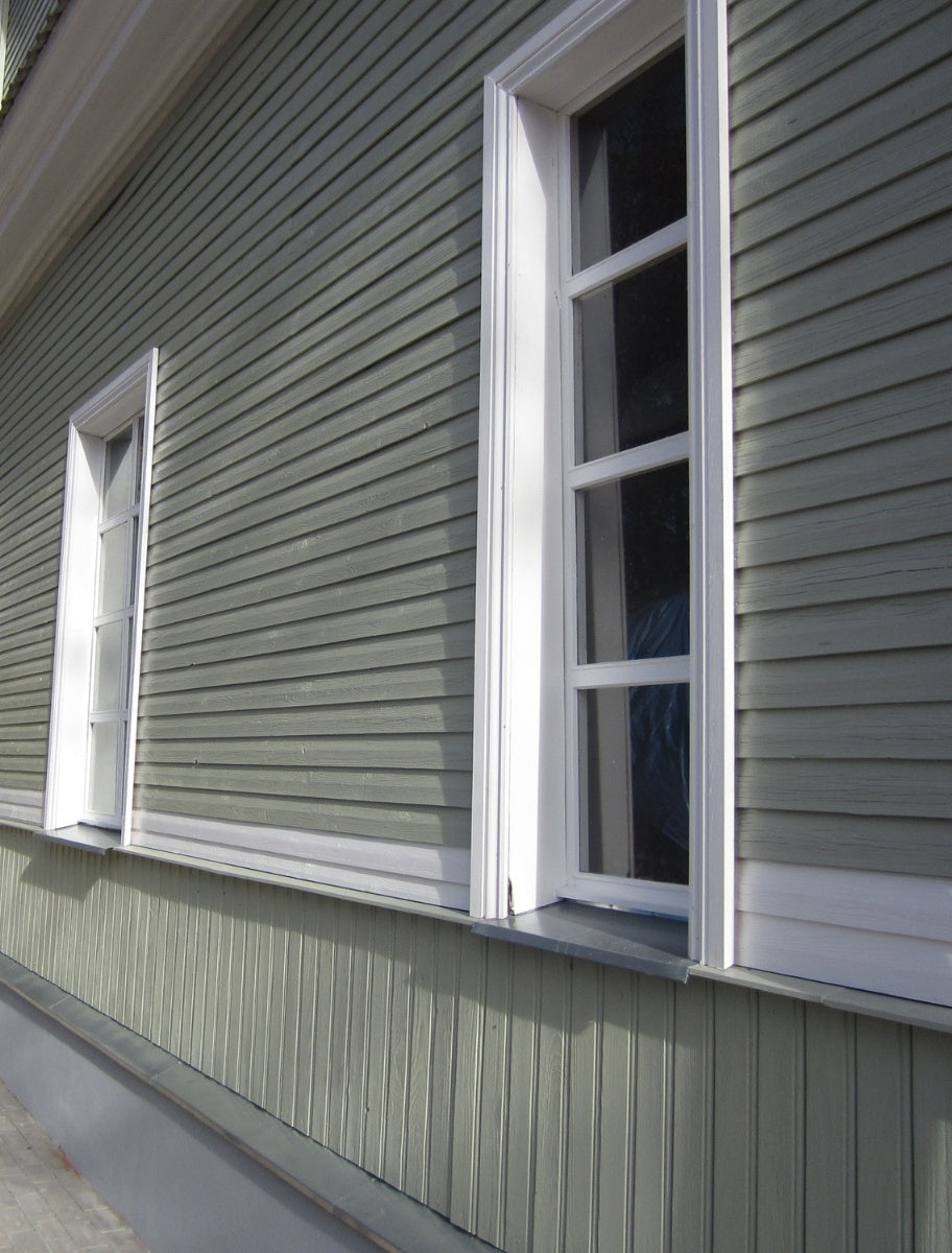A finished wooden house exterior with muted green Paint Eco paint, featuring white-framed windows.