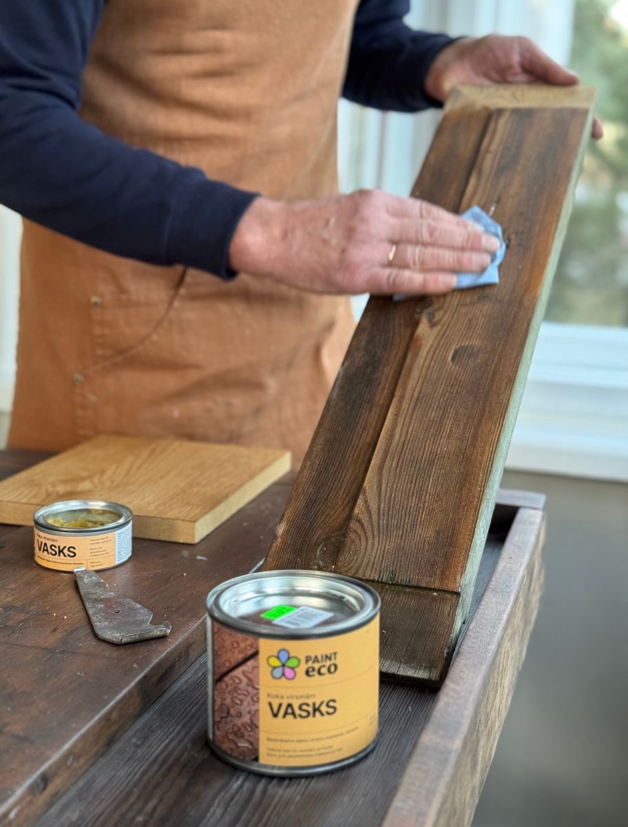A craftsman applying Paint Eco Wax for Wood to a dark wooden board, enhancing its texture and richness. The wax provides protection and a smooth, natural finish.