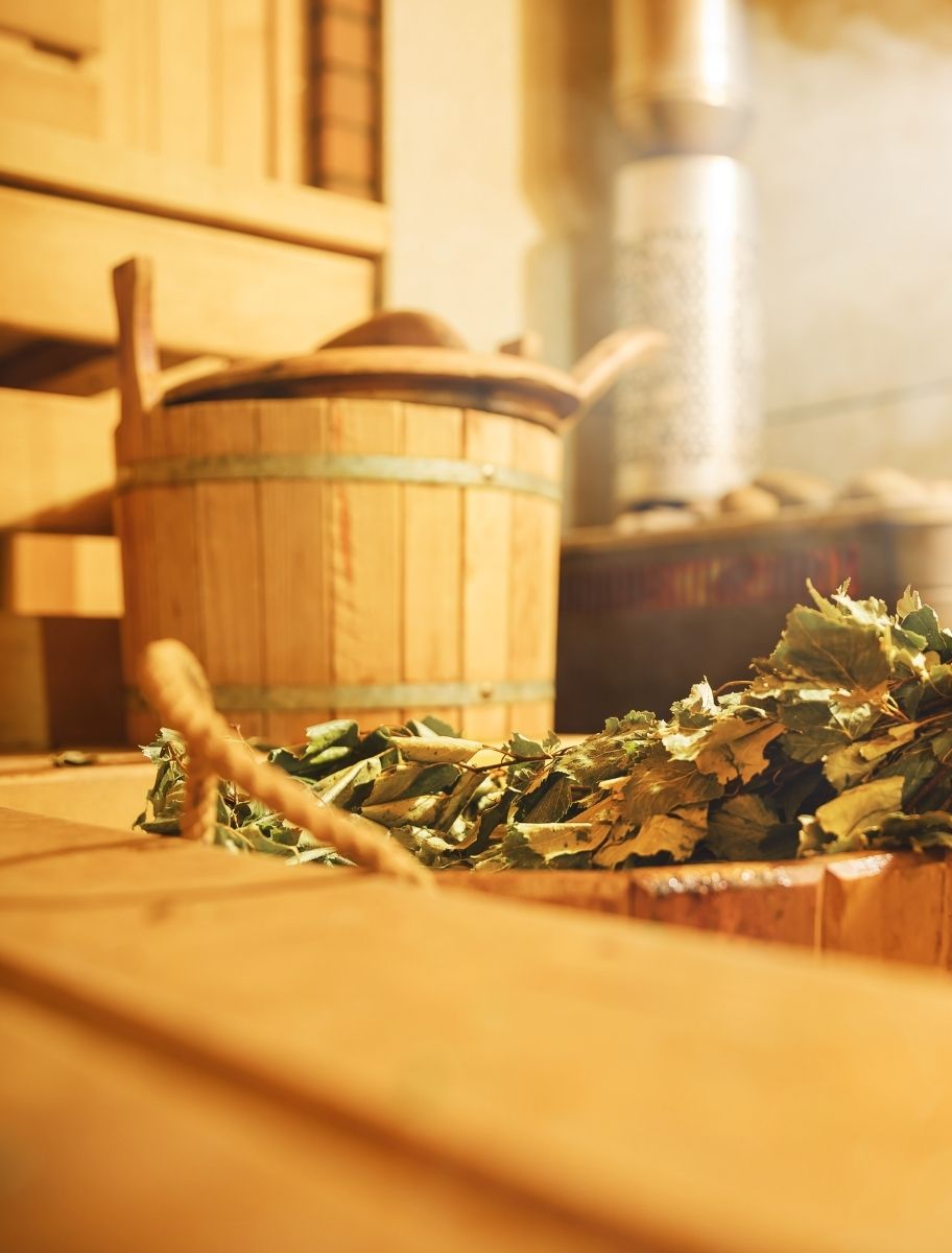 Traditional sauna interior with a wooden bucket, ladle, and dried birch branches on a wooden bench, treated with linseed sauna oil for protection and durability.