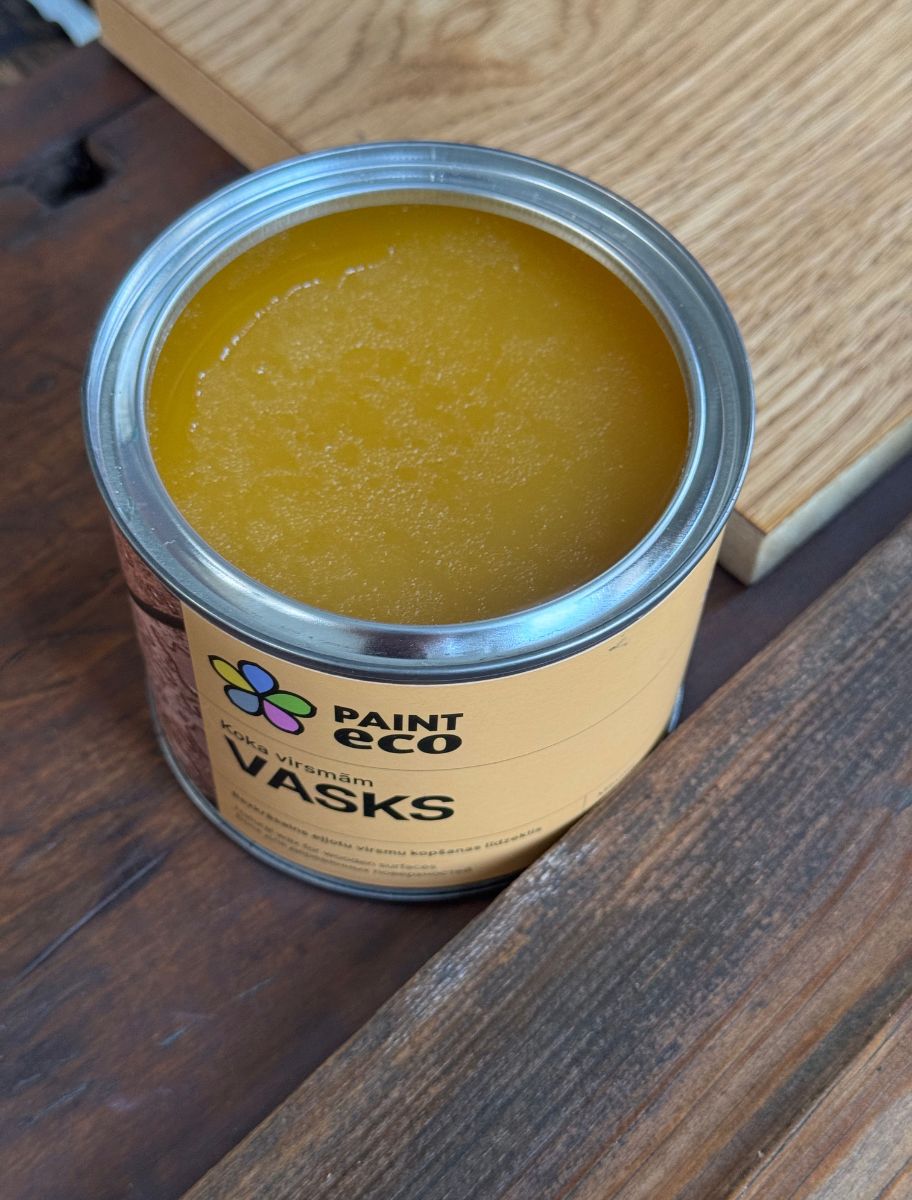 An open can of Paint Eco Wax for Wood with yellowish wax inside, placed on a wooden surface.